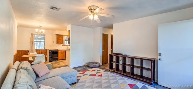 living room with ceiling fan with notable chandelier and wood walls