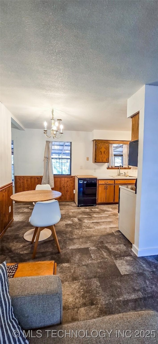 kitchen with a textured ceiling, dishwasher, a chandelier, and wood walls