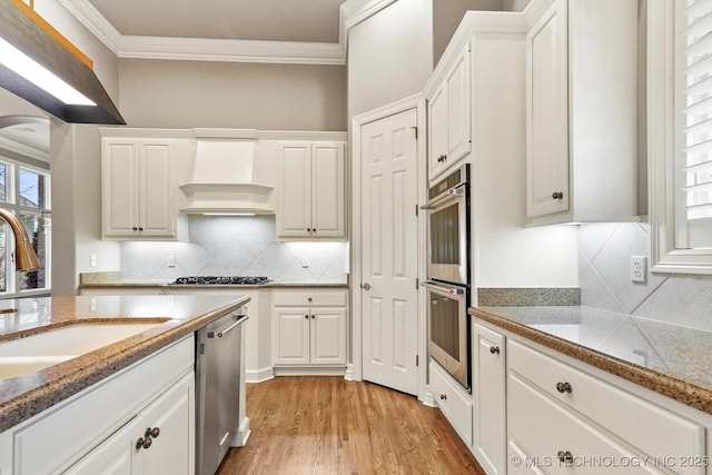 kitchen with ornamental molding, custom exhaust hood, stainless steel appliances, and white cabinets