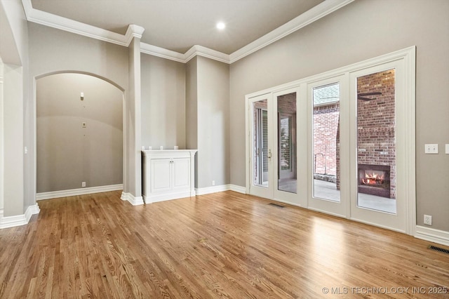 empty room with crown molding, a brick fireplace, and light hardwood / wood-style flooring