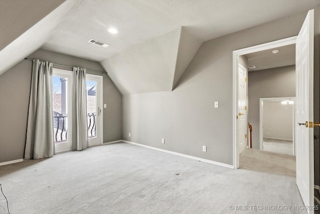 additional living space with vaulted ceiling, light carpet, and a textured ceiling