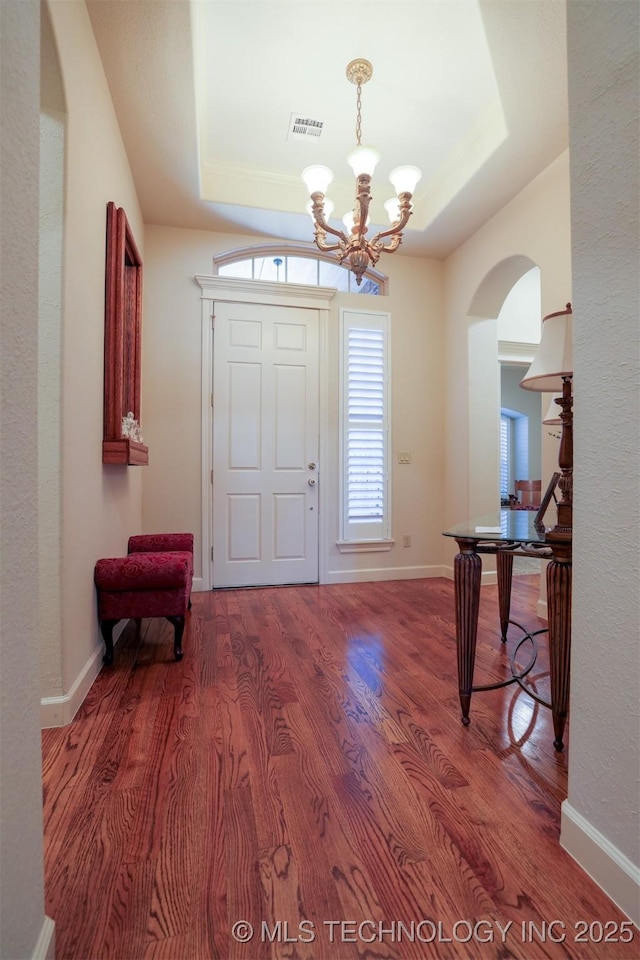 entryway featuring a raised ceiling, hardwood / wood-style flooring, and a notable chandelier