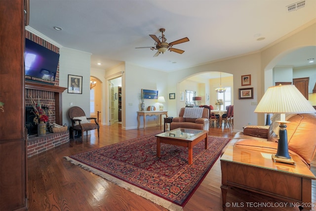 living room featuring crown molding, a brick fireplace, hardwood / wood-style floors, and ceiling fan with notable chandelier