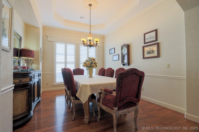 dining room with ornamental molding, dark hardwood / wood-style floors, an inviting chandelier, and a tray ceiling