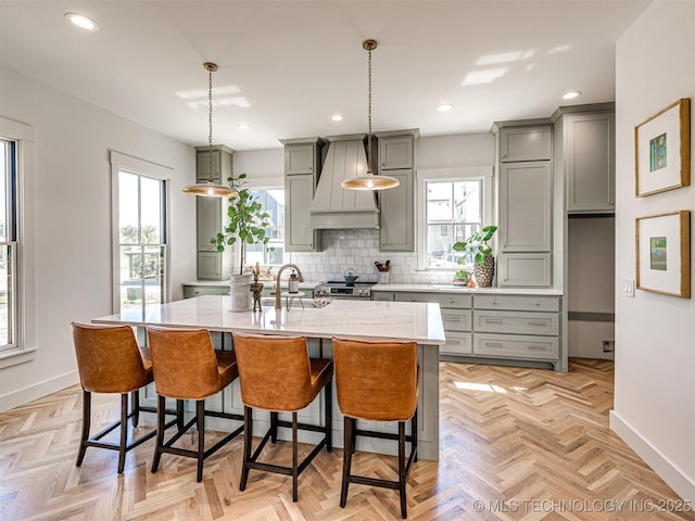 kitchen with premium range hood, a kitchen island with sink, backsplash, and a breakfast bar