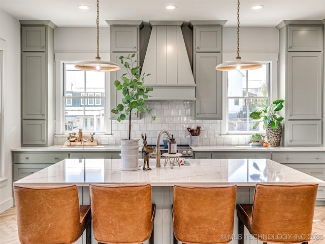 kitchen featuring a kitchen island with sink, hanging light fixtures, custom range hood, and a breakfast bar