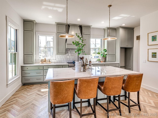 kitchen featuring plenty of natural light, a kitchen island, light stone countertops, a kitchen bar, and light parquet flooring