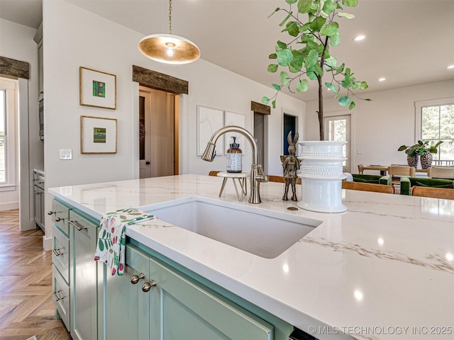 kitchen with pendant lighting, parquet floors, light stone counters, and sink