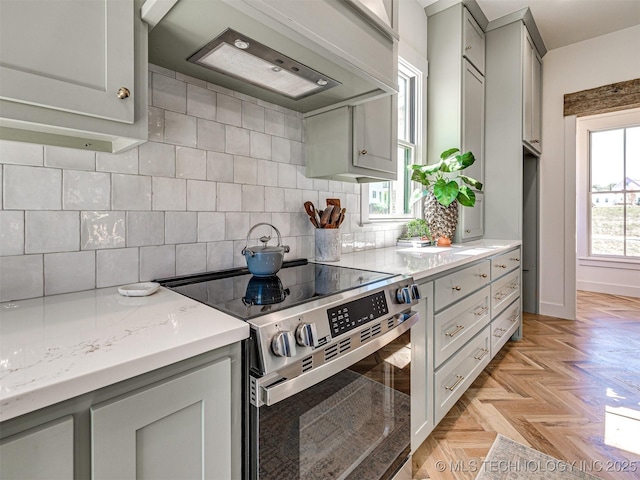 kitchen with premium range hood, stainless steel range with electric cooktop, decorative backsplash, light stone counters, and light parquet flooring