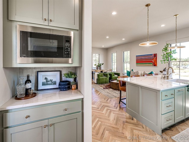 kitchen featuring stainless steel microwave, sink, light parquet floors, hanging light fixtures, and light stone counters
