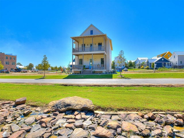 rear view of property featuring a balcony, a yard, and covered porch