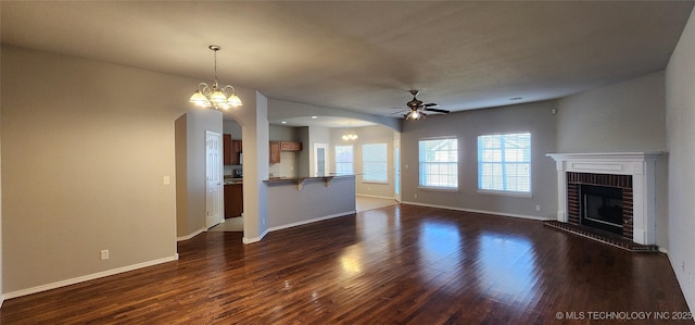 unfurnished living room with dark wood-type flooring, ceiling fan with notable chandelier, and a fireplace