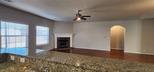 unfurnished living room with dark wood-type flooring, ceiling fan, and a fireplace