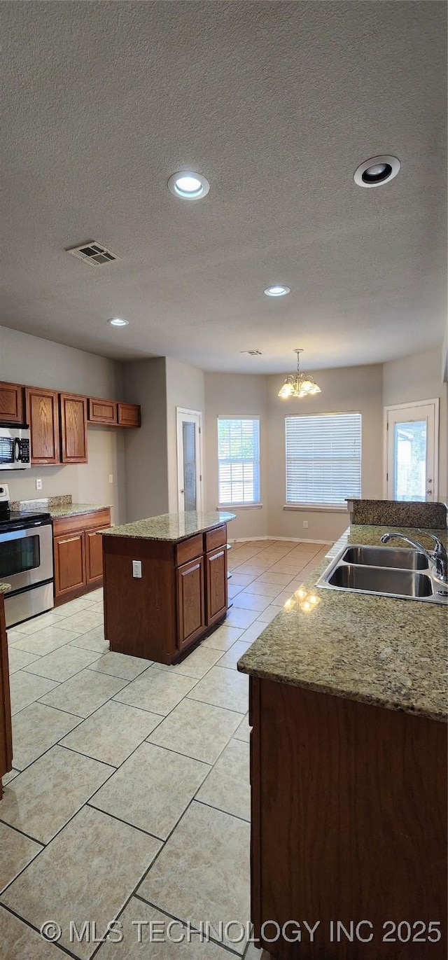 kitchen featuring appliances with stainless steel finishes, sink, a kitchen island with sink, light tile patterned floors, and a textured ceiling