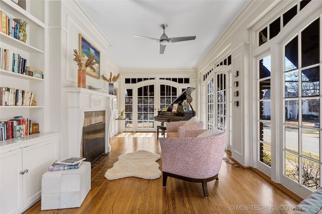 sitting room with built in features, a fireplace, french doors, ornamental molding, and light hardwood / wood-style flooring