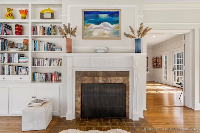 details with built in shelves, crown molding, hardwood / wood-style floors, and a tile fireplace