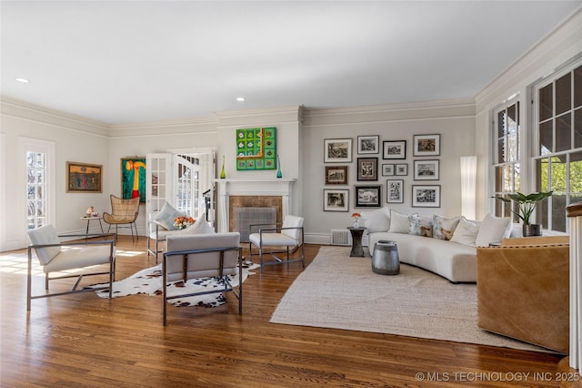 living room featuring a tiled fireplace, wood-type flooring, and ornamental molding