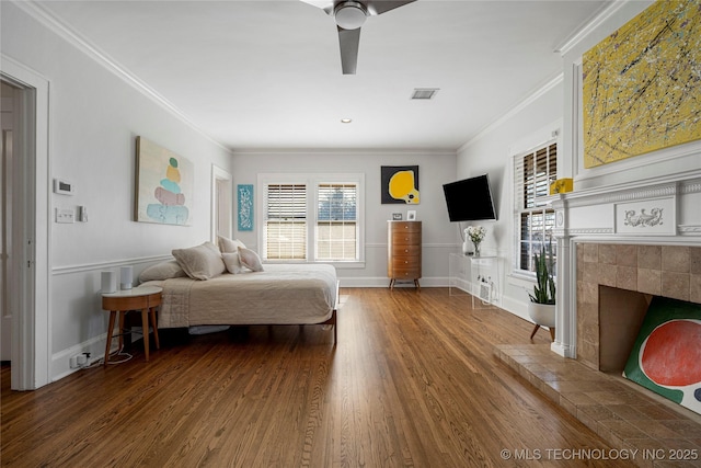 bedroom featuring crown molding, a tiled fireplace, and hardwood / wood-style floors