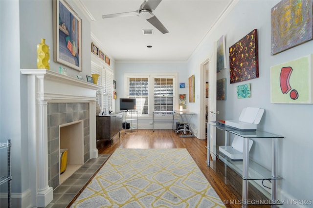 interior space featuring hardwood / wood-style flooring, ornamental molding, a tile fireplace, and ceiling fan