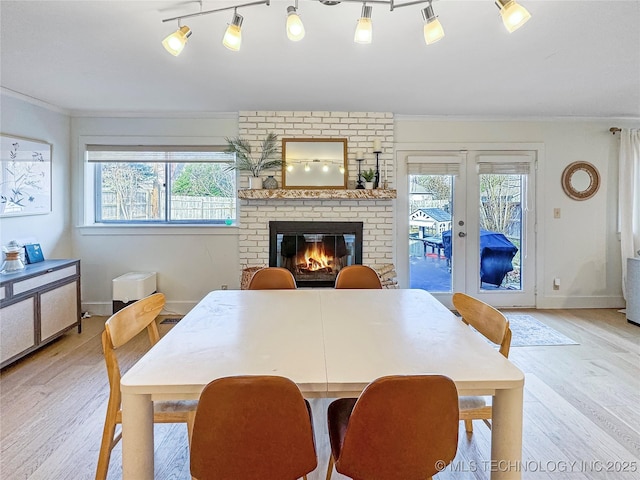 dining space featuring french doors, rail lighting, a brick fireplace, light wood-type flooring, and ornamental molding