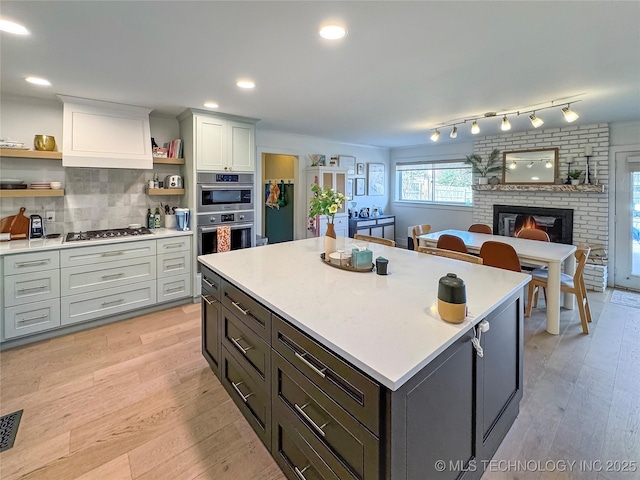 kitchen with stainless steel appliances, a fireplace, a kitchen island, decorative backsplash, and light wood-type flooring