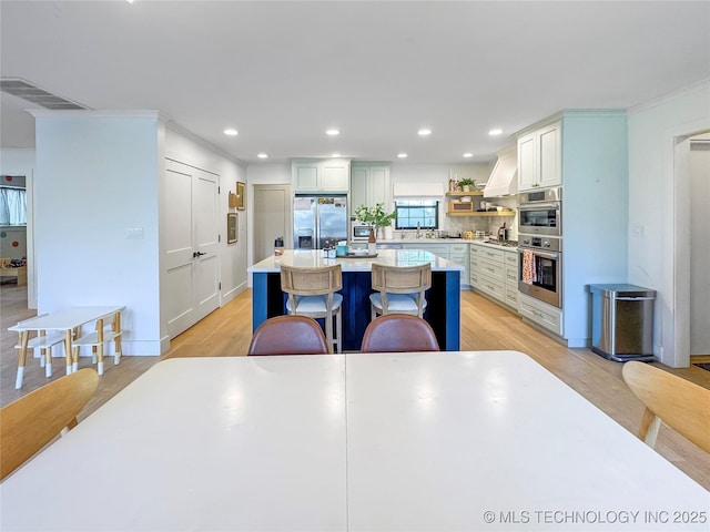 kitchen featuring a breakfast bar, custom exhaust hood, a center island, stainless steel appliances, and white cabinets