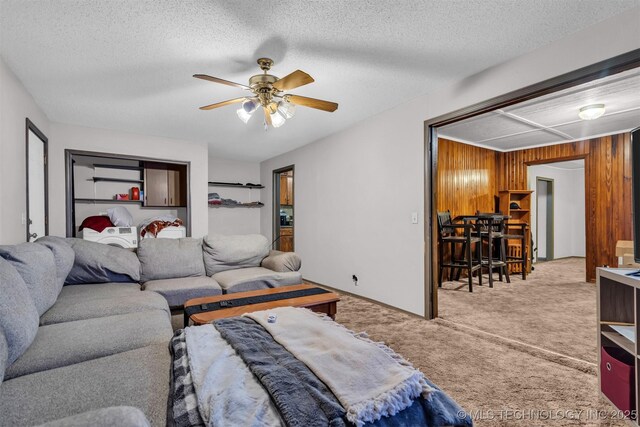 living room with a textured ceiling, wooden walls, ceiling fan, and carpet flooring