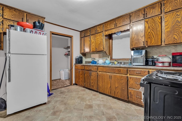 kitchen featuring black stove, tasteful backsplash, sink, white fridge, and crown molding