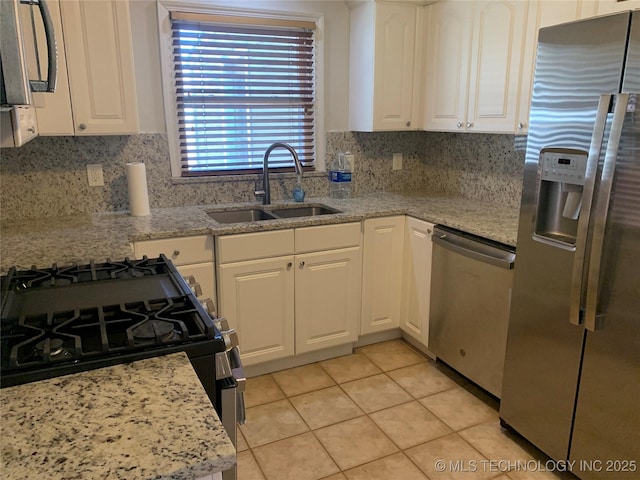 kitchen with appliances with stainless steel finishes, white cabinetry, sink, decorative backsplash, and light stone countertops