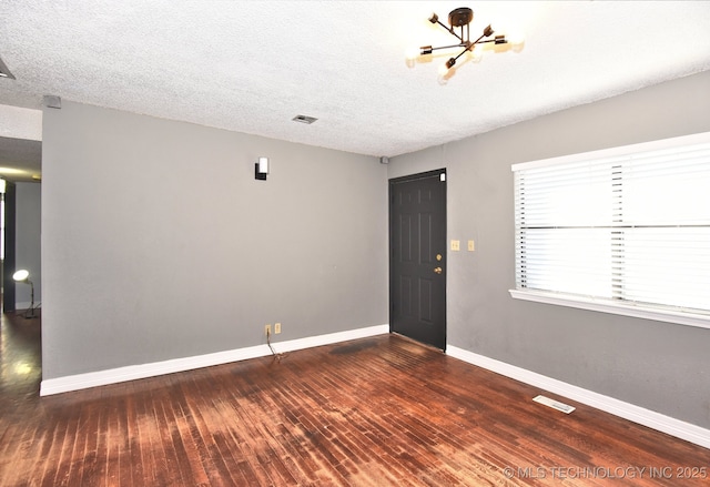 spare room featuring dark hardwood / wood-style floors, a chandelier, and a textured ceiling