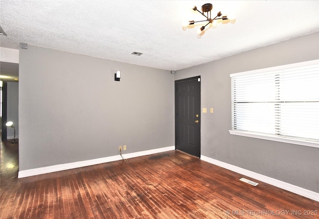 empty room with an inviting chandelier, dark hardwood / wood-style flooring, and a textured ceiling