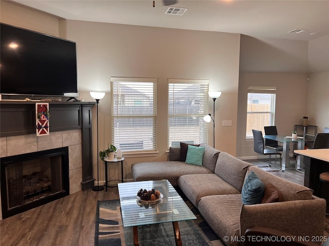 living room featuring a tiled fireplace, visible vents, and dark wood-type flooring