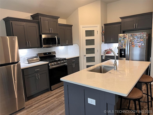 kitchen featuring a kitchen bar, a sink, tasteful backsplash, wood finished floors, and appliances with stainless steel finishes