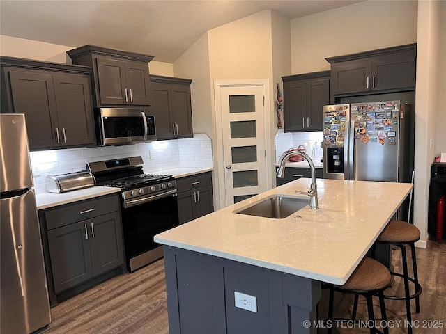 kitchen featuring a kitchen bar, a sink, wood finished floors, stainless steel appliances, and decorative backsplash