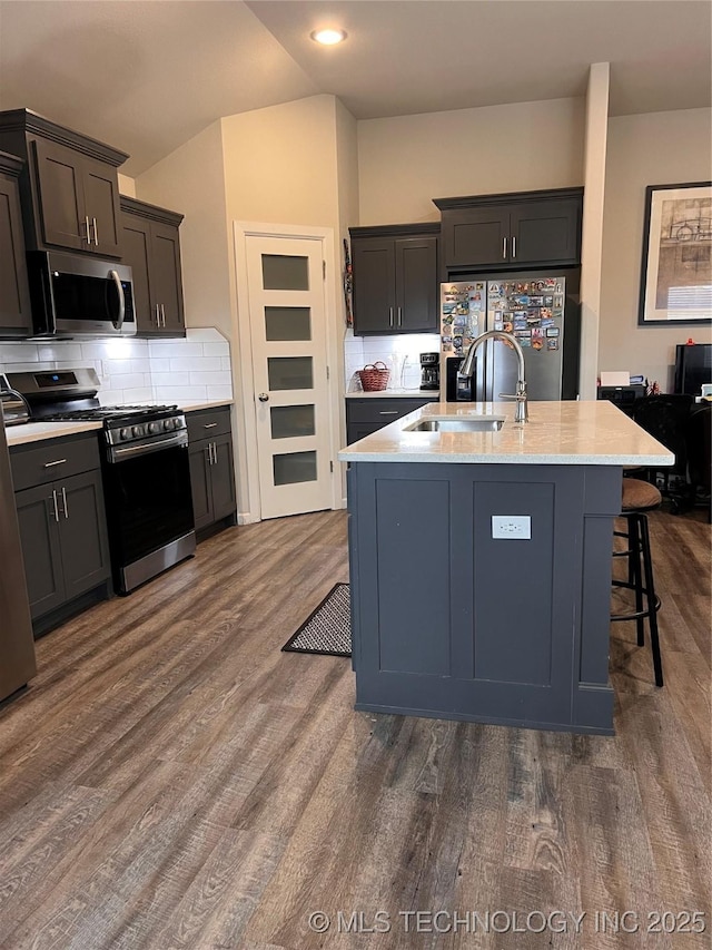 kitchen with a sink, dark wood finished floors, decorative backsplash, stainless steel appliances, and a kitchen island with sink