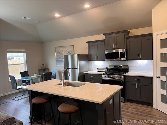 kitchen featuring visible vents, lofted ceiling, a sink, decorative backsplash, and stainless steel appliances