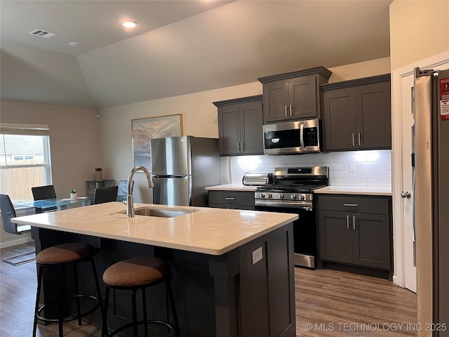 kitchen with visible vents, a sink, vaulted ceiling, appliances with stainless steel finishes, and backsplash