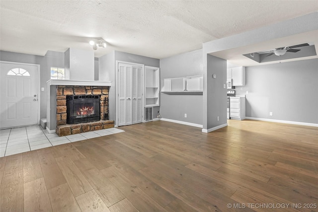 unfurnished living room featuring ceiling fan, a stone fireplace, a textured ceiling, and light wood-type flooring