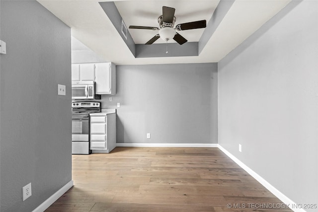 kitchen with white cabinetry, light hardwood / wood-style flooring, appliances with stainless steel finishes, a raised ceiling, and ceiling fan