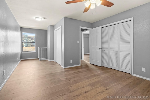 unfurnished bedroom featuring ceiling fan, light hardwood / wood-style flooring, and two closets