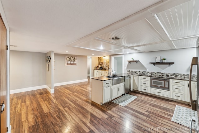 kitchen featuring appliances with stainless steel finishes, sink, white cabinets, hardwood / wood-style flooring, and kitchen peninsula