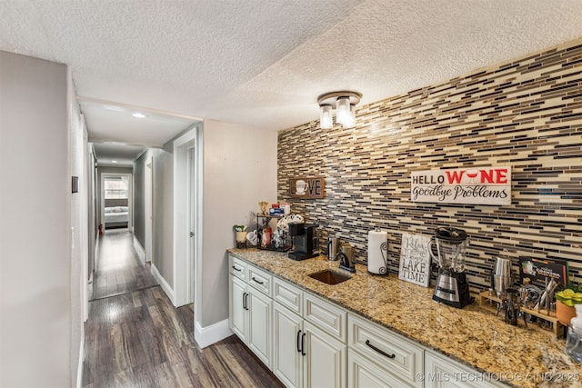 bar with sink, white cabinets, light stone countertops, dark wood-type flooring, and a textured ceiling