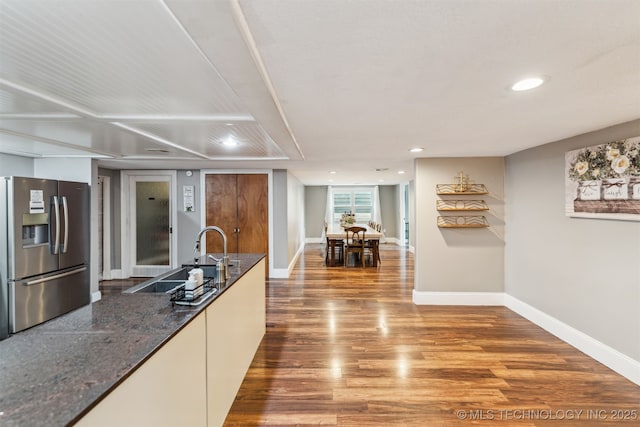 kitchen with stainless steel refrigerator with ice dispenser, sink, white cabinetry, dark stone countertops, and hardwood / wood-style flooring