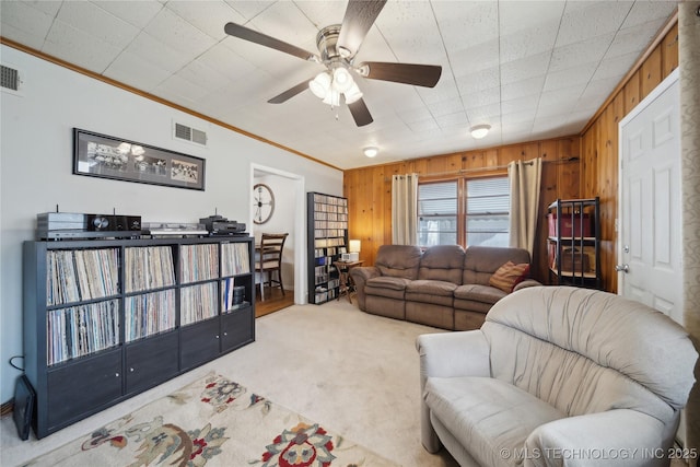 living room featuring ceiling fan, ornamental molding, carpet floors, and wood walls