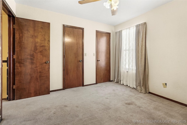 unfurnished bedroom with two closets, light colored carpet, and ceiling fan