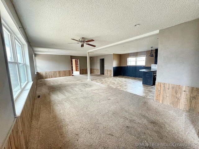 unfurnished living room with ceiling fan, carpet floors, wooden walls, and a textured ceiling