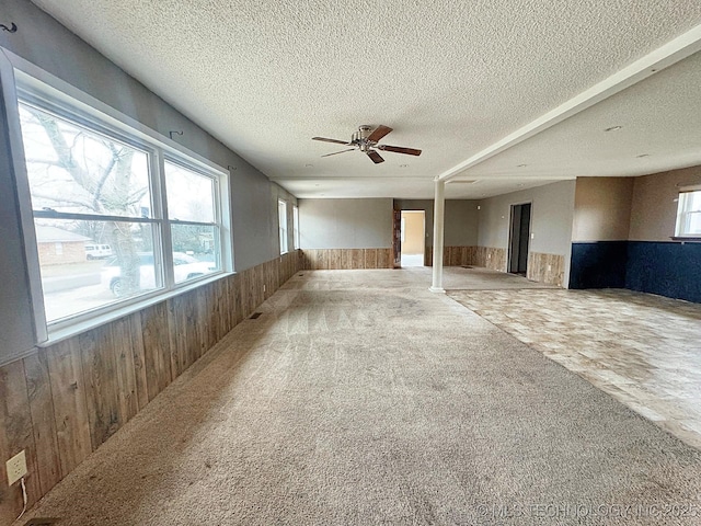 interior space featuring ceiling fan, carpet flooring, a textured ceiling, and wood walls