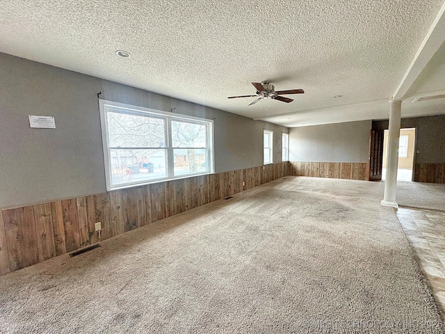 carpeted spare room featuring ceiling fan, a textured ceiling, and wooden walls