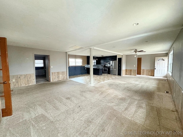 unfurnished living room featuring ceiling fan, light colored carpet, a textured ceiling, and wood walls