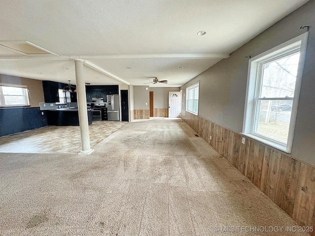 interior space with ceiling fan, wooden walls, carpet flooring, a textured ceiling, and ornate columns